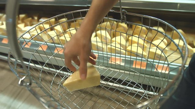 Cheese on the shelf in the supermarket.
Slow motion. The buyer with the basket walks lengthwise the showcase with cheese.
