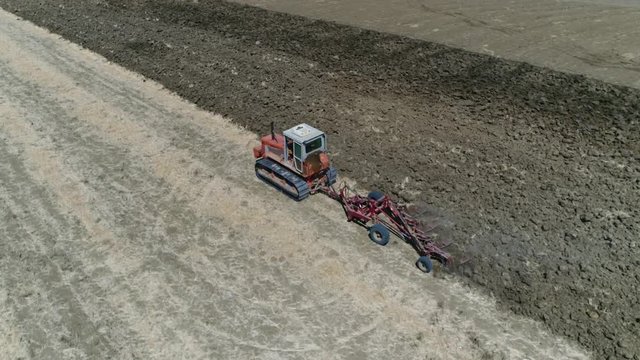 Aerial following tractor on continuous tracks plowing the brown landscape preparing the soil for planting crops because of steep uphill route these tank tracks or caterpillar tracks are needed 4k
