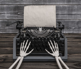 Hands of the skeleton prints on a vintage typewriter. Empty sheet of old paper for your ad design text