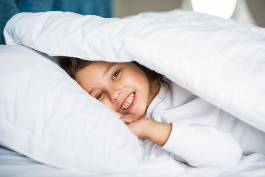Pretty little girl in sleepwear lying under blanket in the bed at home