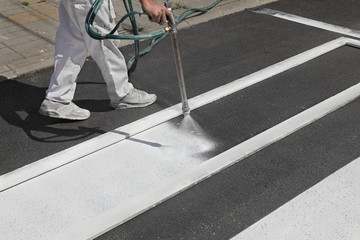 Worker spraying pedestrian crosswalk at a street