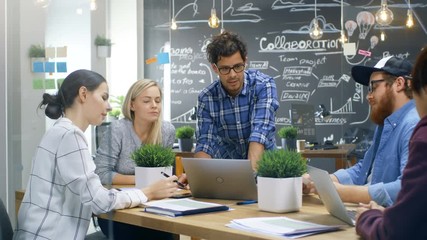 Charismatic Team Leader Shows Laptop to a Diverse Group of Talented Young Developers, They Start Discussion at the Meeting Table