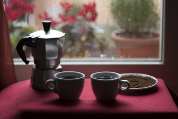 Cups of Hot Coffee and Espresso Machine in front of window raindrops