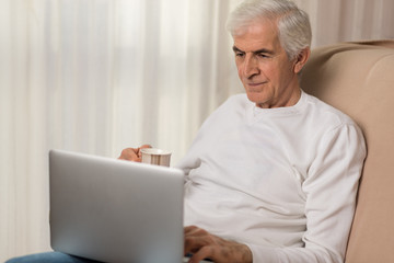 Fototapeta premium Mature man using laptop during coffee time at home