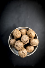 A bowl of whole walnuts in their shells in a bowl shot from above on a natural black slate background