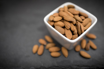 A white bowl of healthy and nutritious almonds shot from above on a black slate background