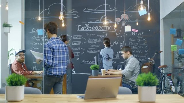 Long Shot of The Busy Office Where Young Creative People Work on Personal Computers, Draw Project Outline on Blackwall and Have Discussions with Colleagues. Shot on RED EPIC-W 8K Helium Cinema Camera.