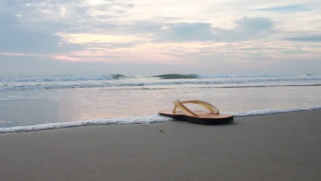 Old flip flops on nobody sandy beach near sea waves in morning. Summer vacation concept