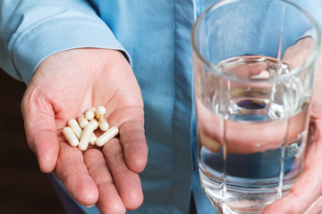 White medication capsules of glucosamine, healthy supplement pills in woman palm hand and glass with water in the other hand