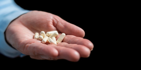Fototapeta premium White medication capsules of glucosamine, healthy supplement pills in woman palm hand, on black background