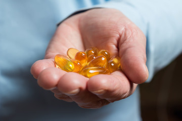 Yellow medication capsules of omega 3, fish oil, healthy supplement pills in the woman palm hand