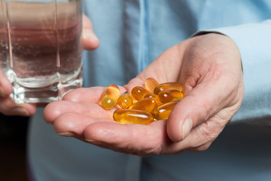 Yellow medication capsules of omega 3, fish oil, healthy supplement pills in the woman palm hand and glass with water in the other hand