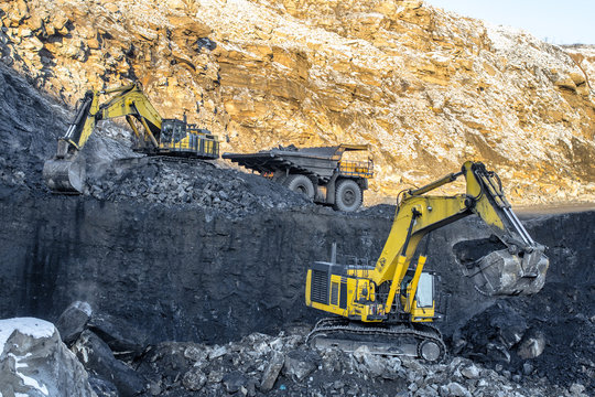 Big yellow dump truck and excavator in coal mine at sunrise 
