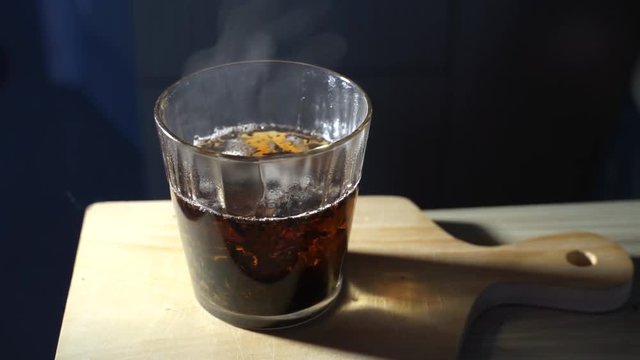 Pour three teaspoons of sugar into a glass of hot tea water. A glass of hot tea with tea leaves in the glass.