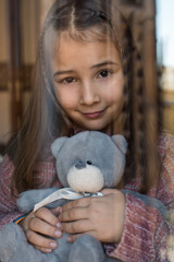 Portrait of a young cute little girl looking throughout the window with teddy bear.
