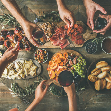 Flat-lay of friends hands eating and drinking together. Top view of people having party, celebrating together at vintage wooden rustic table set with different wine snacks and fingerfoods, square crop