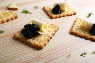Cracker with butter and black caviar on a wooden background