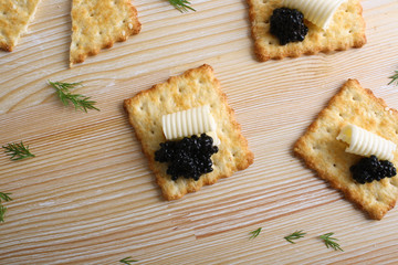 Obraz na płótnie Canvas Cracker with butter and black caviar on a wooden background