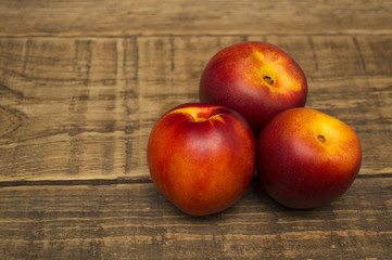 Fruit, three ripe appetizing nectarines on a wooden table