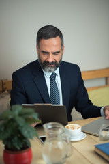 Senior older business man using a computer while sitting in a coffee shop