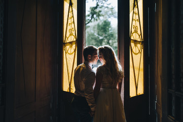 A silhouette of a couple in a doorway with a back light. The newlyweds at the open doors hold hands and kiss.