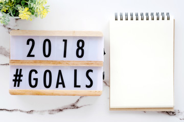 2018 goals on wood box and blank notebook paper on white marble background, business new year aim...