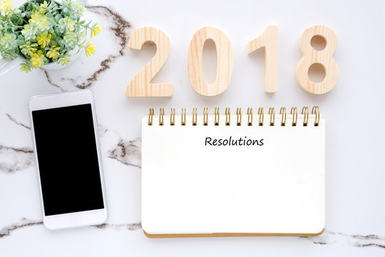 2018 resolutions on blank notebook paper and smart phone on white marble background, new year concept, template