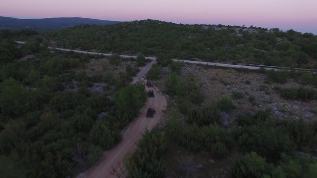 Drone shot of dune buggies driving offroad on a dirt road in sunset