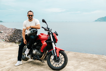 Fototapeta na wymiar Rider sitting on his motorbike, holding helmet on sea background