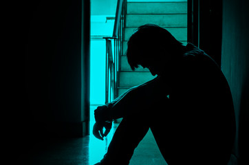 Silhouette of man sitting alone,Sad and Serious Man sitting hug his knee alone of close condo., Dramatic moment. with copy space