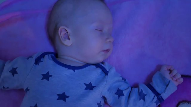 Sleeping newborn baby in bed. Smiling in a dream, a beautiful little boy is sleeping sweetly.