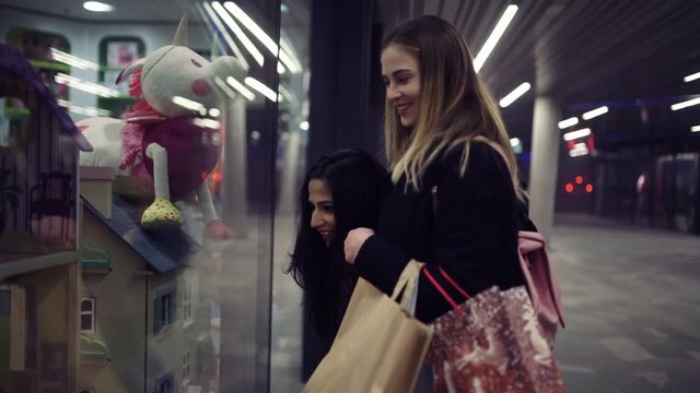 Two cute young adolescent women, heavy loaded with christmas gifts,  shopping, while walking along store windows and choosing and admiring the items. 