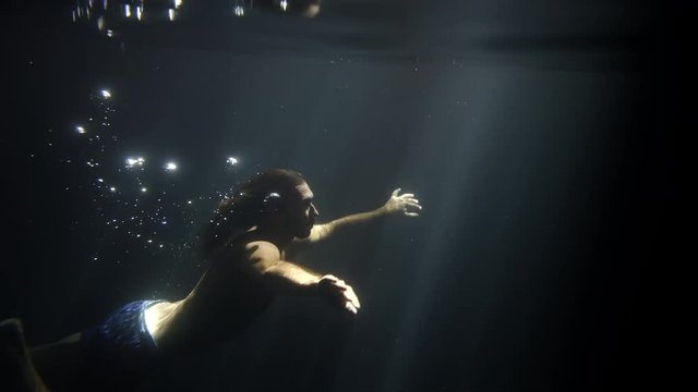 Man swiming underwater in sun rays and bubbles and surface in light, cenote cave in tulum