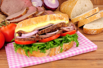 Roast beef salad sandwich with ingredients on a wood background