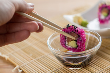 Frau isst Pink gefärbte California Inside Out Lachs Avocado Sushi mit Sojasoße