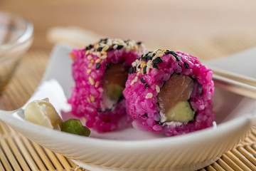 Zwei Pink Inside Out Sushi mit Lachs, Avocado und Frischkäse mit Sojasoße und Holz Stäbchen