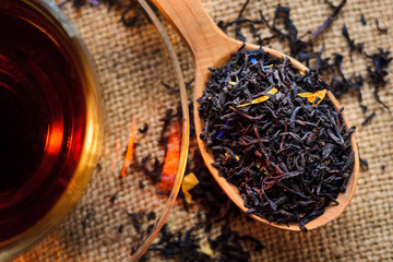 Tea leaves in a wooden spoon next to a cup of brewed tea on a background of burlap