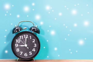 Fototapeta na wymiar Black alarm clock with flying snow on blue background.