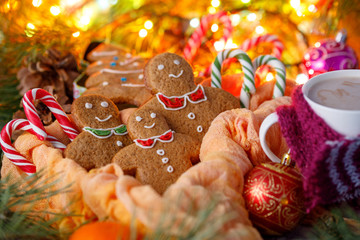 Fototapeta na wymiar Biscuits in the form of little men for Christmas and hot drink cocoa on a background of a garland and a box in the form of a Christmas tree. Christmas tale.