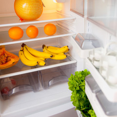 Open fridge with fruit and greens inside on white shelves. The concept of a healthy diet.