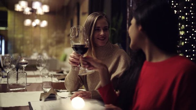 Two adolescent women going through the menue  in a fancy restaurant, while drinking a glass of red wine and laughing and talking, maybe gossiping