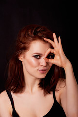 Fototapeta premium Girl in Studio on dark background. Red hair, great figure. Shows a positive gesture that everything is cool. Life is beautiful and positive