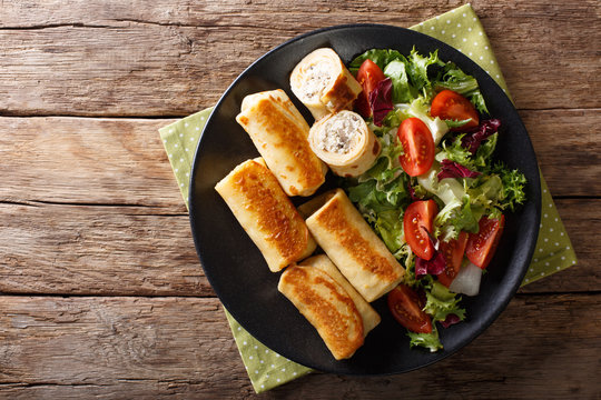 Tasty crepes rolls with chicken and mushrooms and vegetable salad on a plate close-up. Horizontal top view