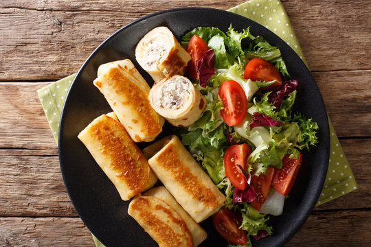 crepes rolls with chicken, cheese and mushrooms close-up and salad of fresh vegetables. horizontal top view