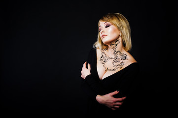 Fototapeta premium Studio portrait of blonde girl with originally make up on neck, wear on black dress at dark background.