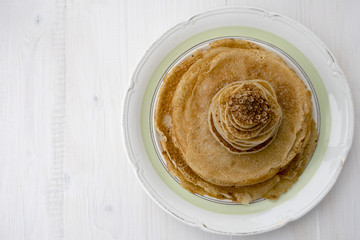Large and small pancakes are located on a light wooden table. Close-up and place for copy space.