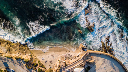 Drone view of waves hitting the rocks and the beach at seashore alongside a park in La Jolla San Diego