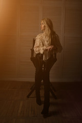 Blond business woman in retro casual lace dress. Beautiful girl with curly hair and cream top sitting on a wood chair in photo studio