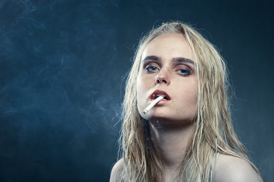 sad young blond woman on dark blue background smoking