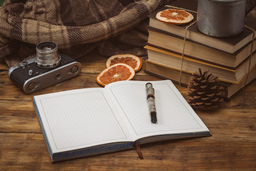 Diary with pen, books, aluminum antique cup with hot tea and an old camera, orange slices and plaid on a wooden background. Shot at an interesting angle.